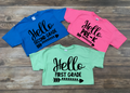 Three youth t-shirts in blue, pink, and light green displaying Hello Pre-K, Hello First Grade, and Hello Second Grade text with arrow graphic.
