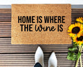 A natural coir doormat with the text Home Is Where The Wine Is positioned in a rustic entryway.