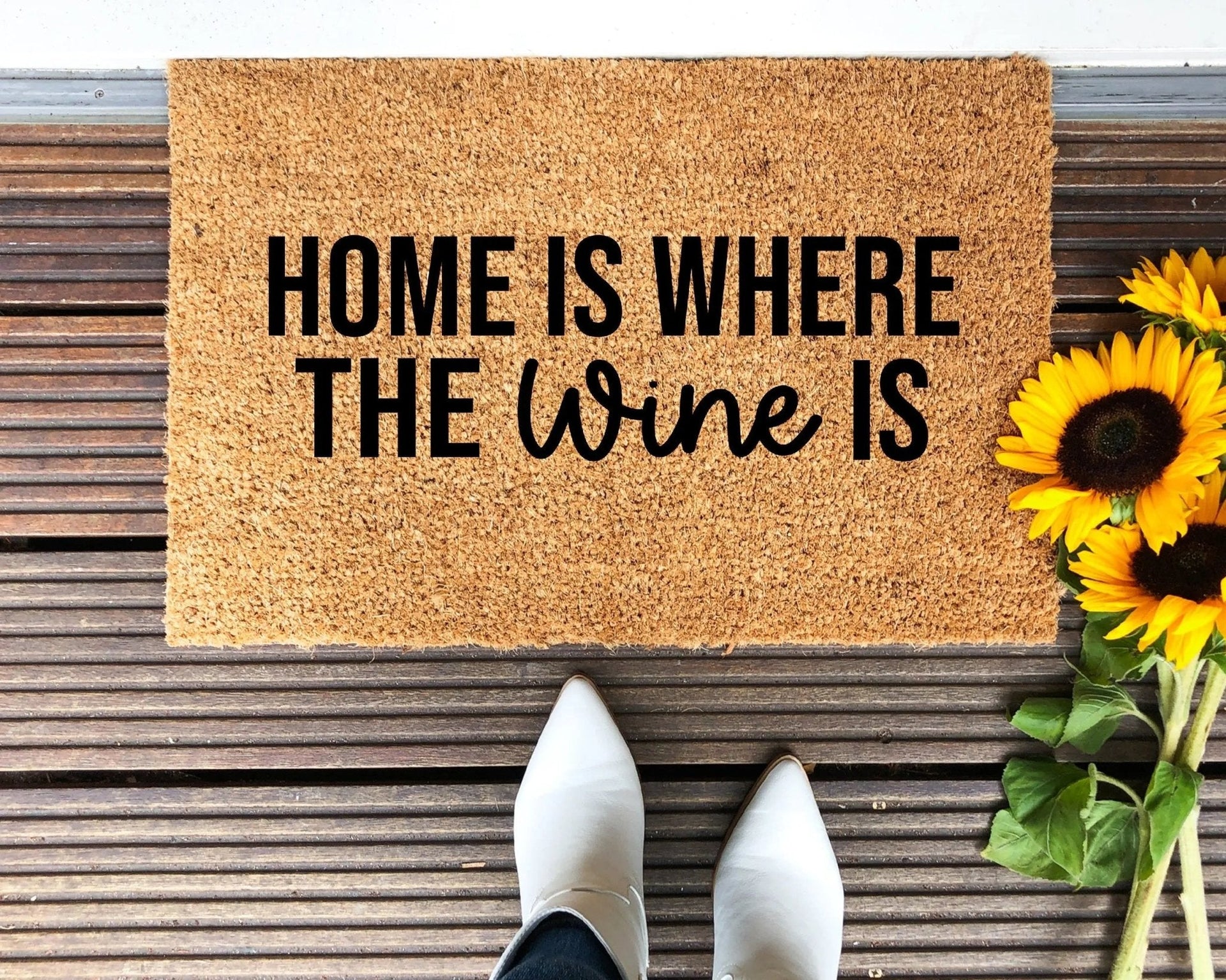 A natural coir doormat with the text Home Is Where The Wine Is positioned in a rustic entryway.