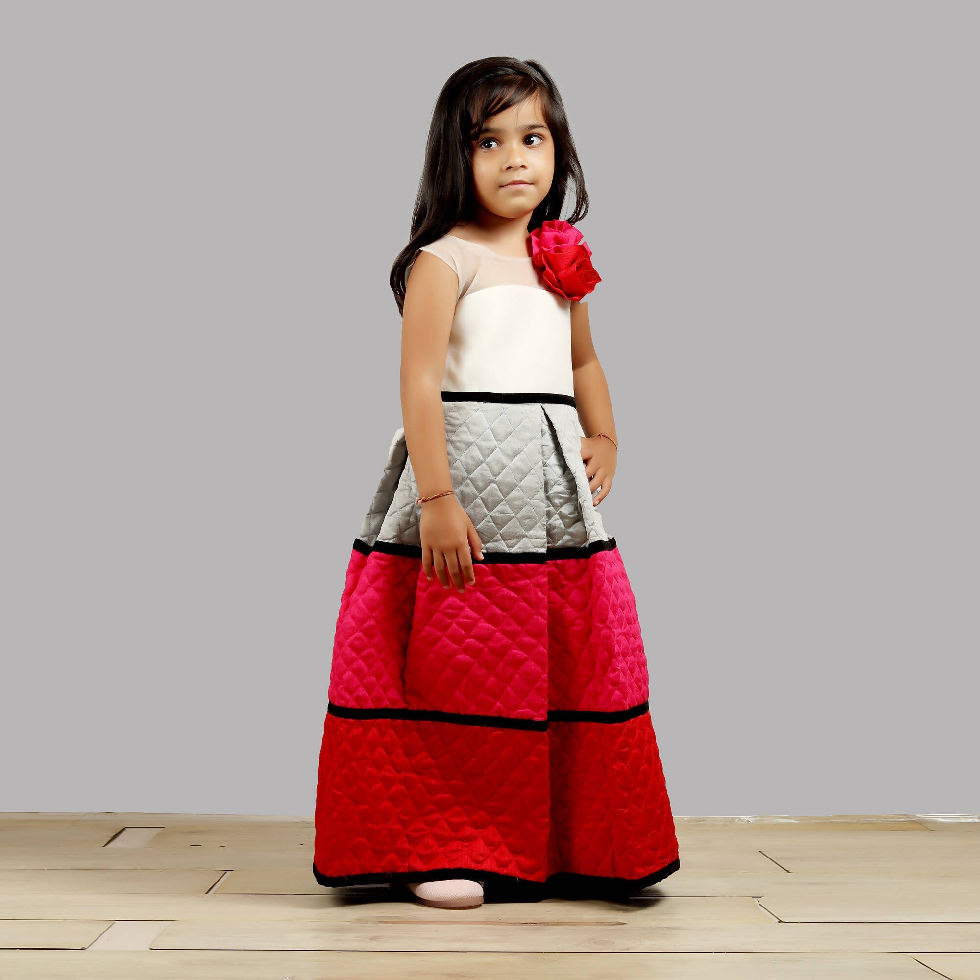 A stylish girls dress with a white bodice and a quilted multicolor skirt featuring black accents.