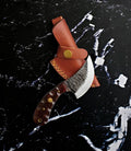 Hand forged Ulu inspired skinning blade with brown handle and brass accents on a rustic background.