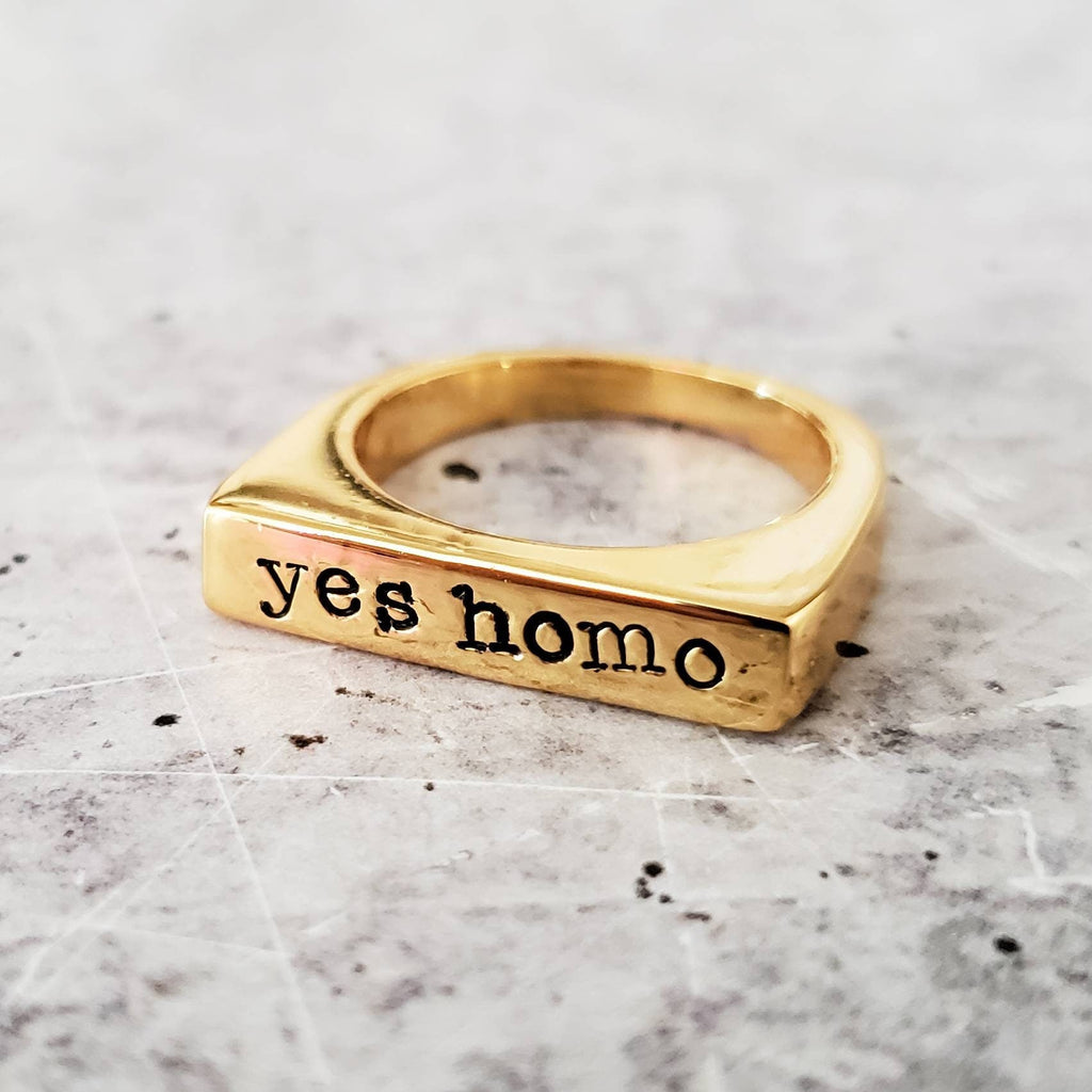 Gold-tone flat-top ring with the words yes homo stamped in typewriter font