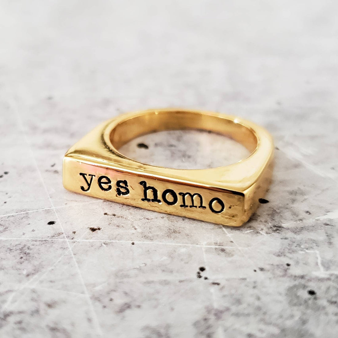 Gold-tone flat-top ring with the words yes homo stamped in typewriter font