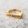 Gold-tone flat-top ring with the words yes homo stamped in typewriter font