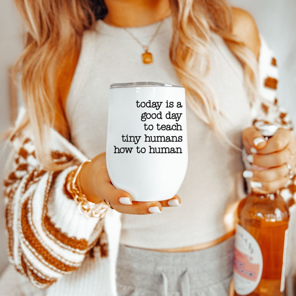 White stainless steel tumbler with the text Today is a good day to teach tiny humans how to human held by a person.