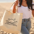 Person holding a tote bag with a beach design and text on a sandy background