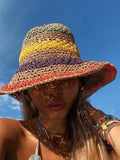 A woman wearing a vibrant rainbow striped braided straw fisherman hat with a wide brim against a blue sky background.