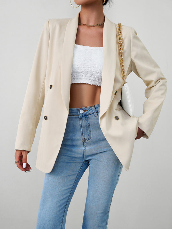 A woman wearing a beige double-breasted blazer over a white crop top and blue jeans.