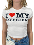A woman wearing a white short-sleeve crop top with a black and red I heart my boyfriend graphic print.