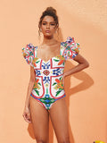 Model wearing a white one-piece swimsuit with colorful enamel-inspired floral patterns and ruffled sleeves.