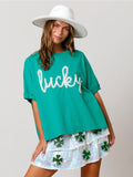 A woman wearing a loose-fitting kelly green graphic t-shirt with the word lucky in textured script across the chest.