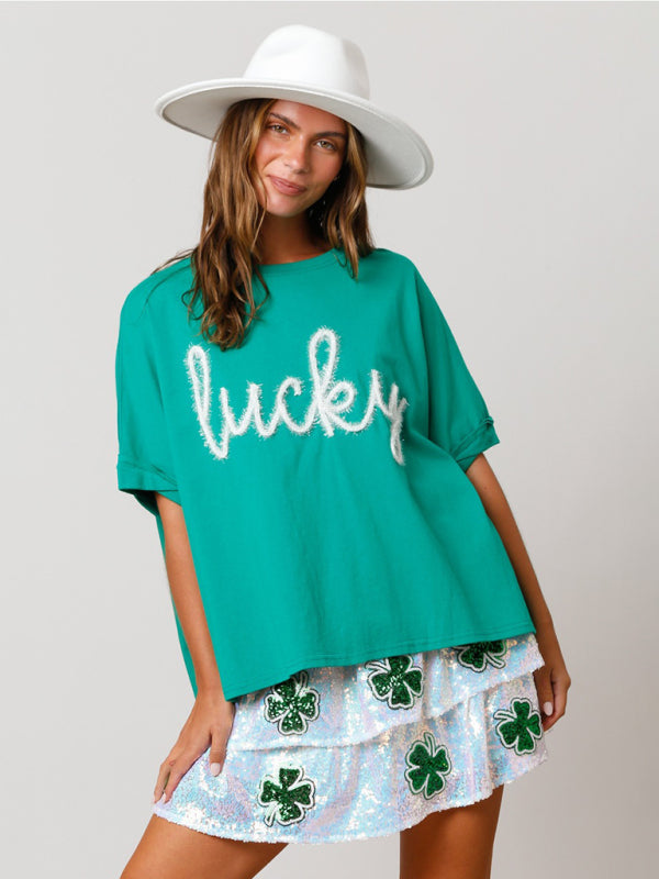 A woman wearing a loose-fitting kelly green graphic t-shirt with the word lucky in textured script across the chest.