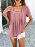 A woman wearing a mauve short-sleeve square neck top with a floral eyelet pattern and front pleats.