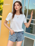 A woman wearing a crisp white round neck short sleeve t-shirt, styled casually with denim shorts.