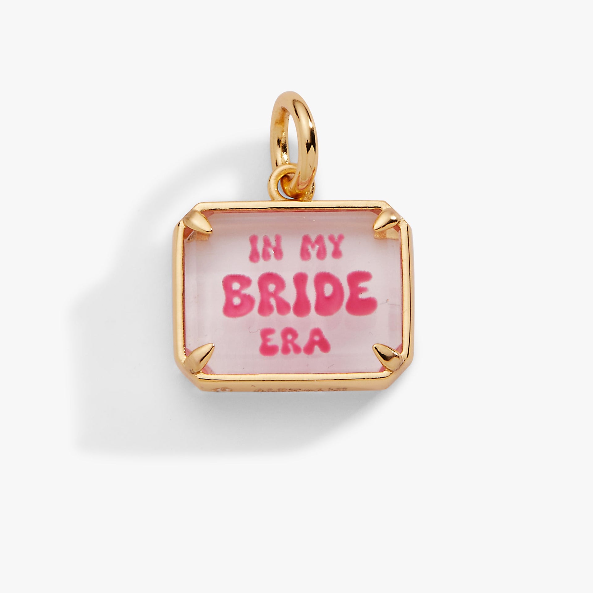 A polished gold rectangular charm with pink enamel text that reads In My Bride Era and a faceted resin stone.