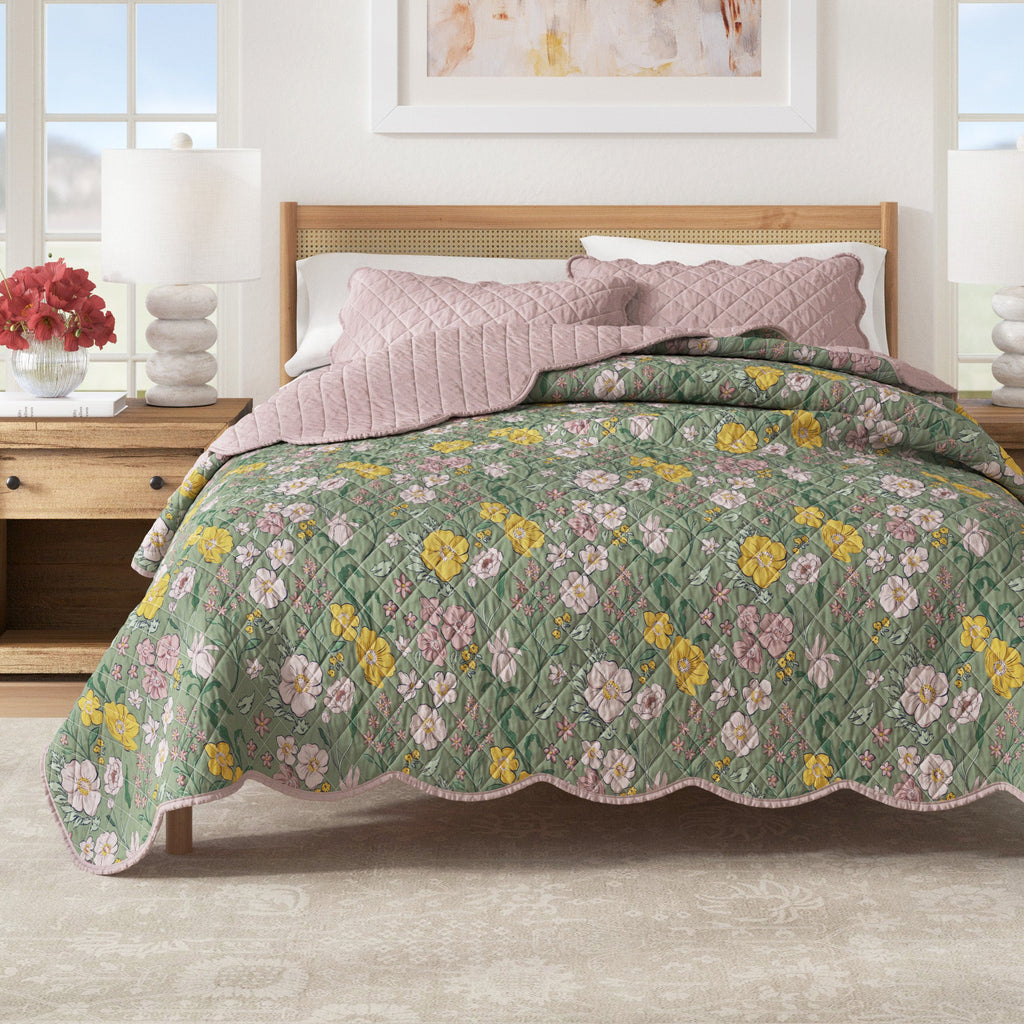 Floral print quilt with scalloped edges and a reversible solid pink side on a bed