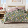 Floral print quilt with scalloped edges and a reversible solid pink side on a bed