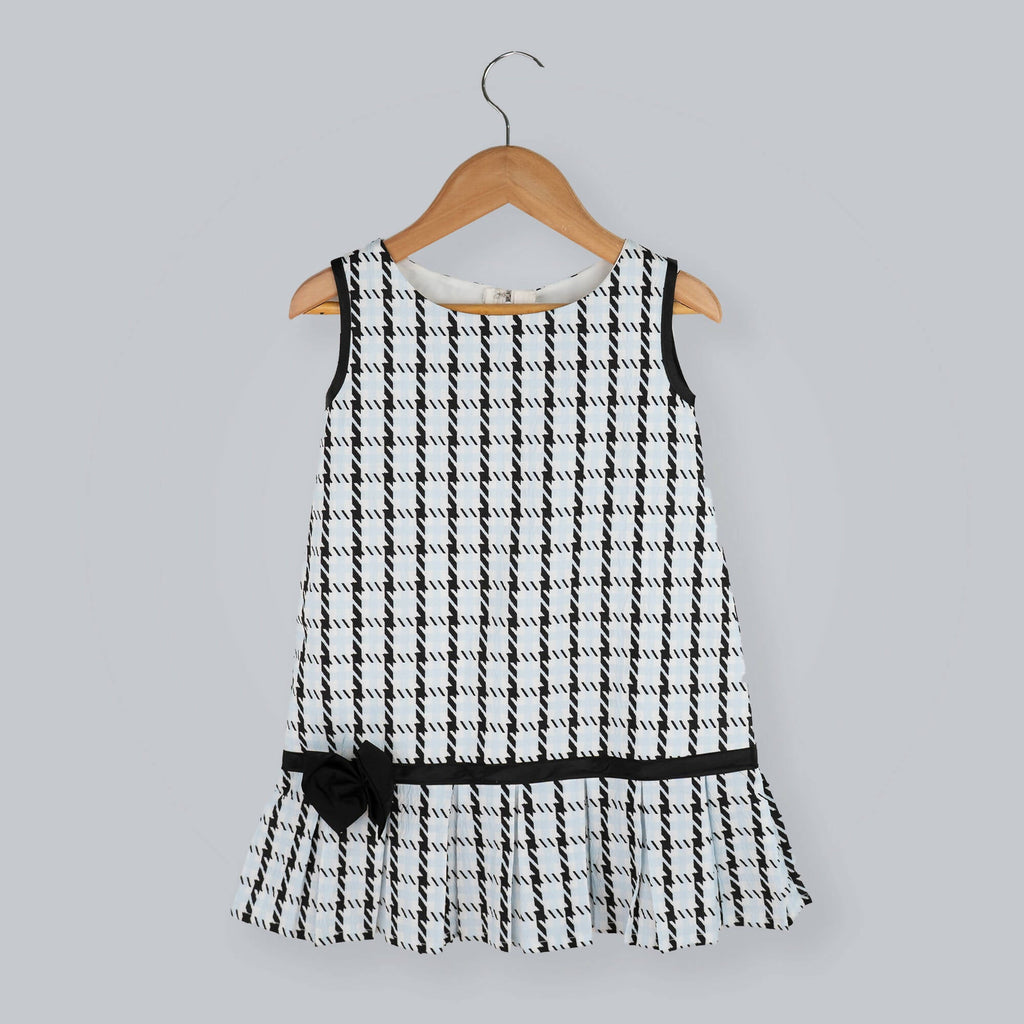 Girl's sleeveless black and white box print A-line dress with a black taffeta bow at the hem.
