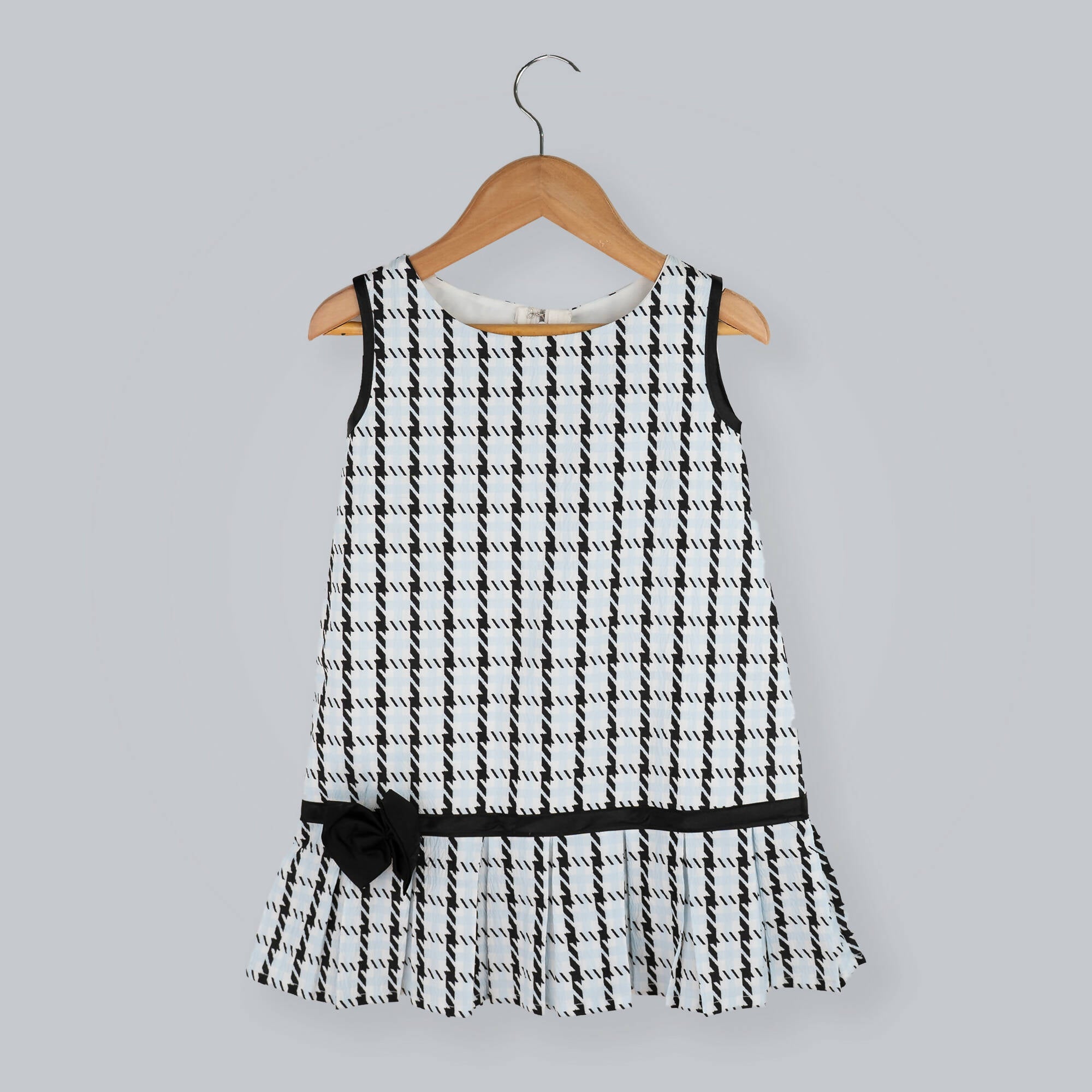 Girl's sleeveless black and white box print A-line dress with a black taffeta bow at the hem.