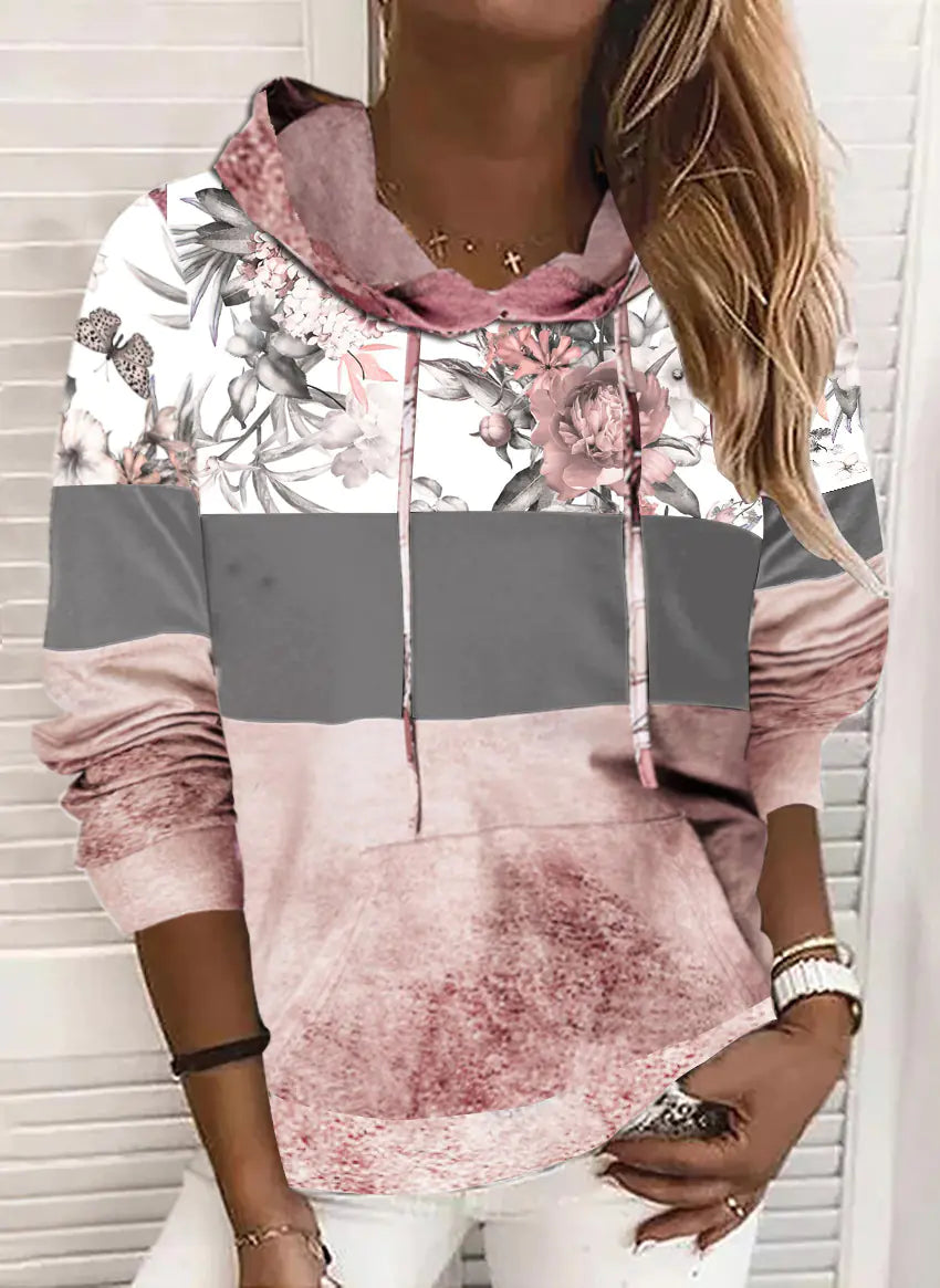 A woman wearing a stylish long-sleeve floral and colorblock fleece hoodie with a kangaroo pocket.