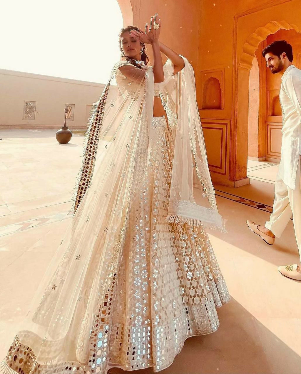 Woman wearing a cream georgette lehenga choli with intricate paper mirror and thread embroidery.