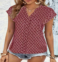 A woman wearing a deep red V-neck blouse with a white geometric print, featuring short sleeves and a relaxed fit.