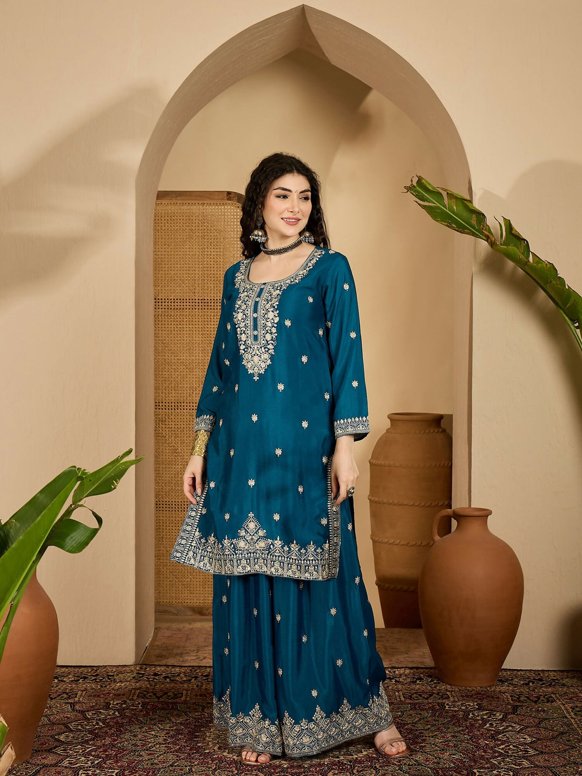 A woman wearing a teal Chinon silk kurta set with intricate embroidery and 3/4 sleeves.