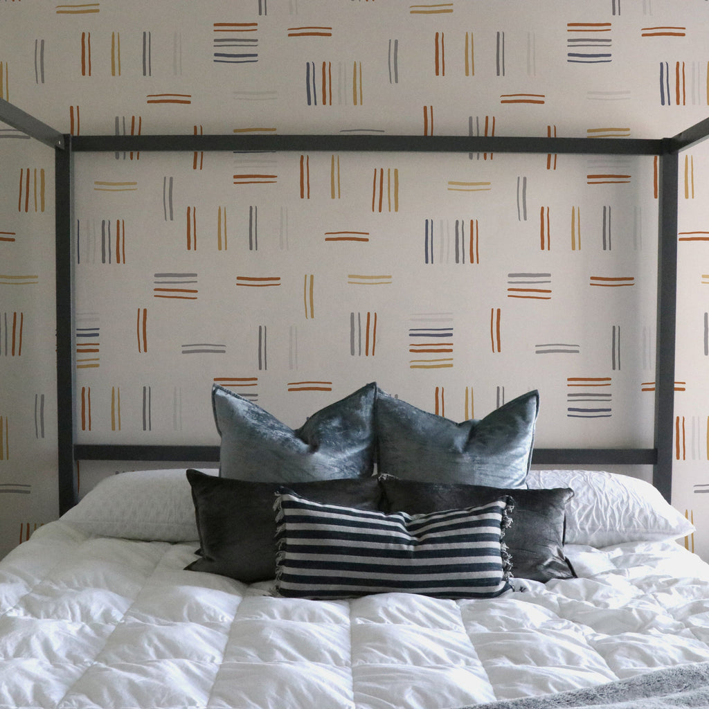 Keren geometric wallpaper in terracotta, mustard, and slate blue on a white wall in a modern boho living room.