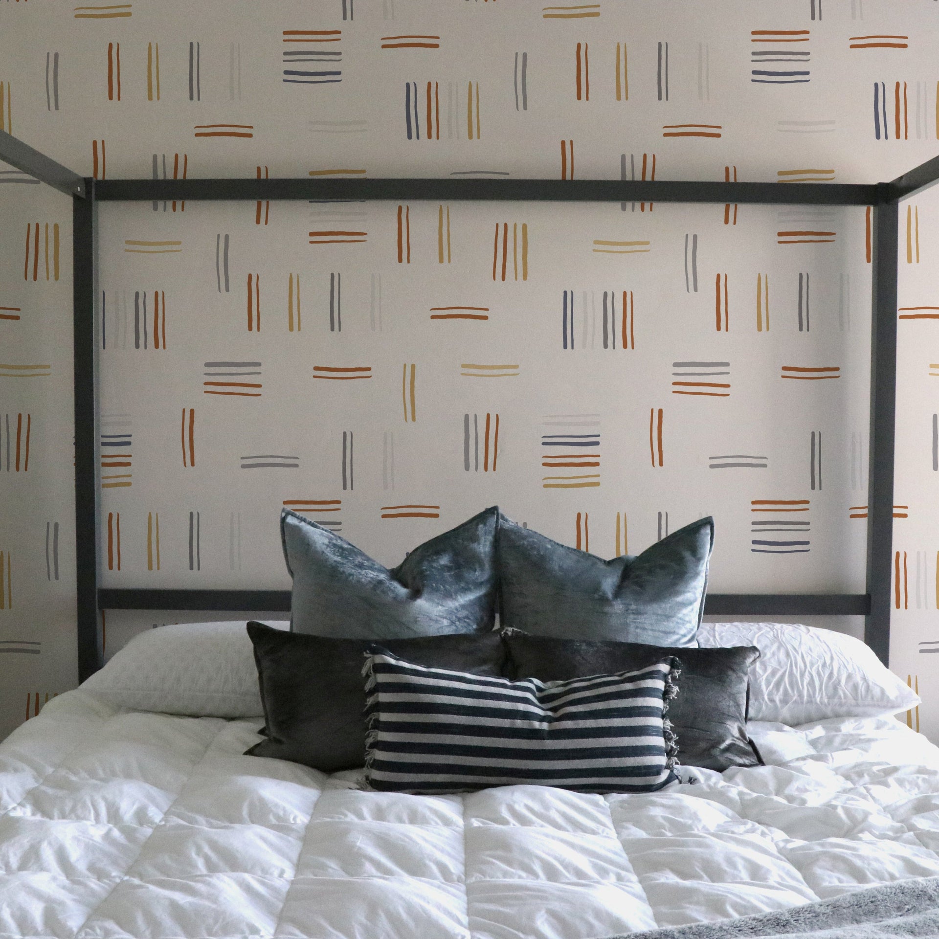 Keren geometric wallpaper in terracotta, mustard, and slate blue on a white wall in a modern boho living room.