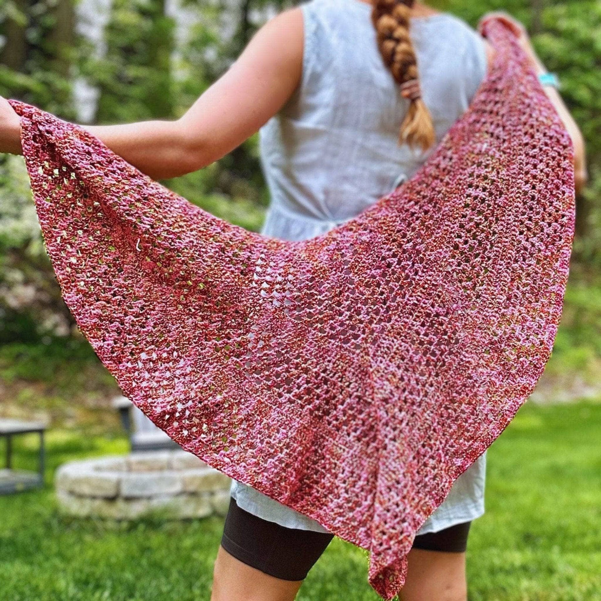 A colorful crocheted shawl in pink, green, yellow, orange, and teal displayed in a garden setting.