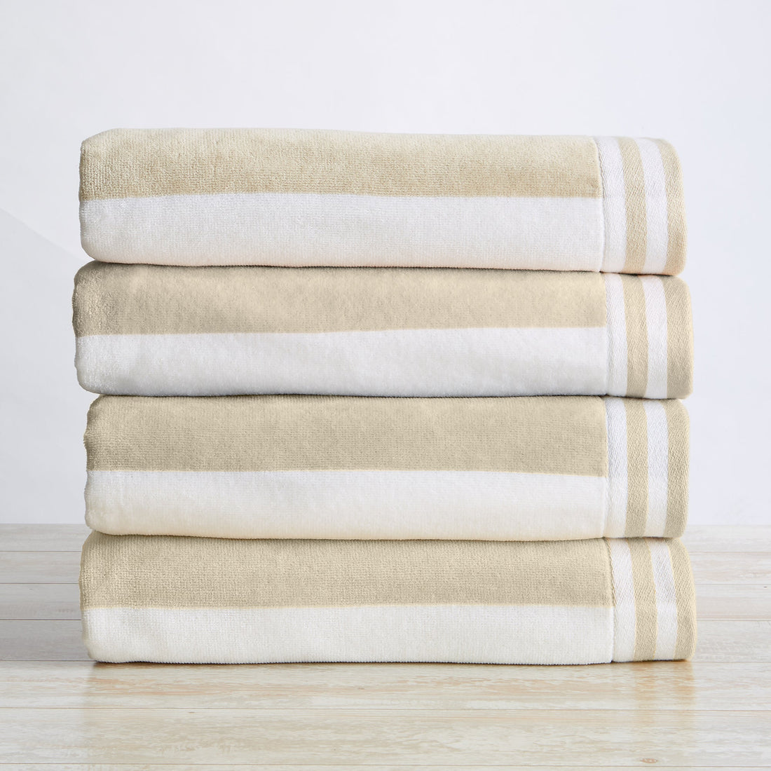 A stack of folded 100% cotton cabana-style beach towels with white and beige stripes and detailed border texture.