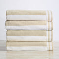 A stack of folded 100% cotton cabana-style beach towels with white and beige stripes and detailed border texture.