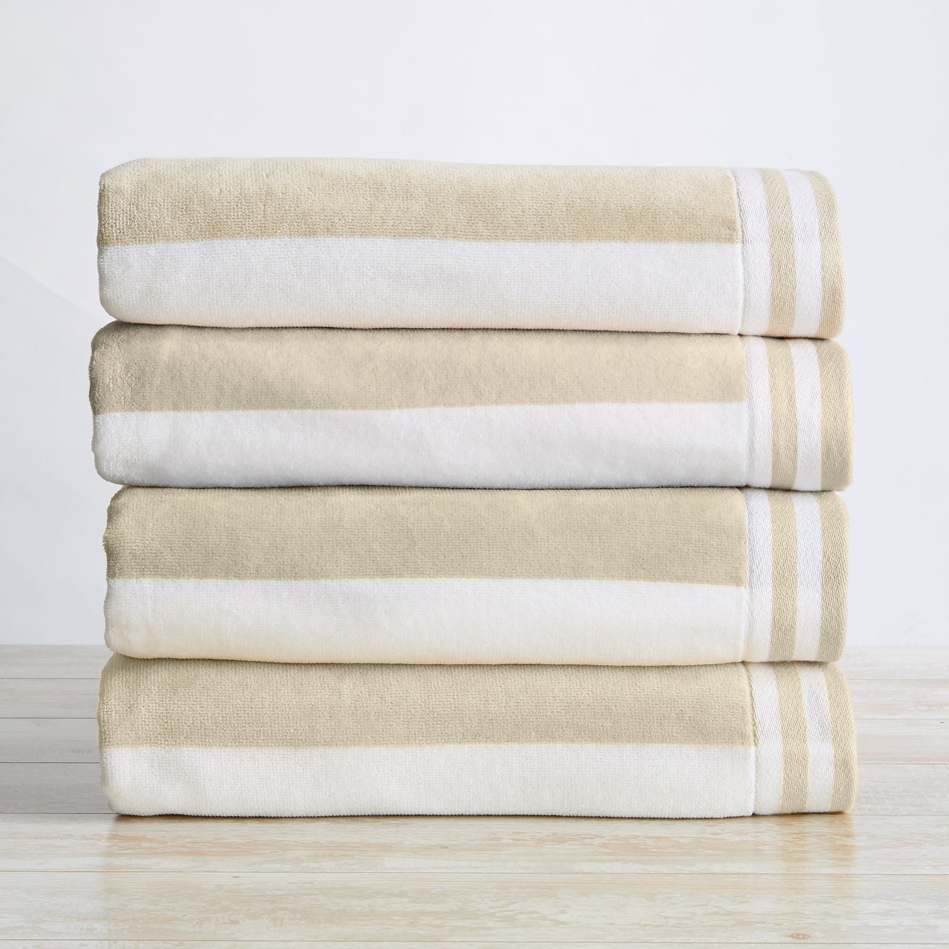 A stack of folded 100% cotton cabana-style beach towels with white and beige stripes and detailed border texture.