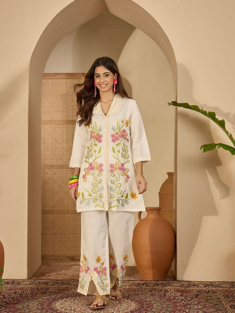 Woman wearing a cream colored Roman Silk stitched kurta with embroidery and shirt collar paired with matching pants.