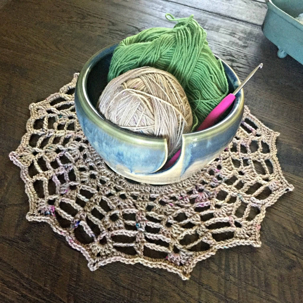 A finished intricate crocheted beige doily with multicolor flecks displayed as vintage tabletop decor.
