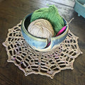 A finished intricate crocheted beige doily with multicolor flecks displayed as vintage tabletop decor.