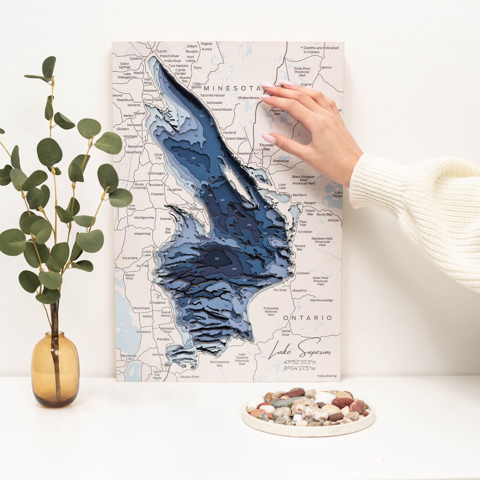 Layered wooden map of Lake Superior featuring blue bathymetric depths and white wood details hanging on a wall.