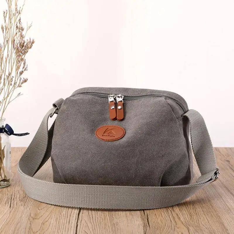 Minimalist canvas crossbody bag in beige worn as a shoulder bag, showing leather patch detail.