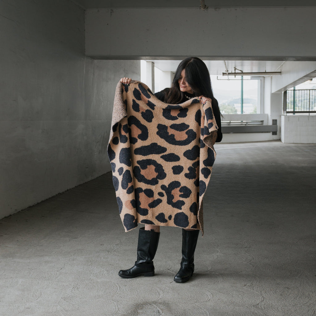 Modern earth-toned leopard print knit throw blanket draped over a neutral sofa in a cozy living room