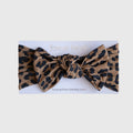 Baby wearing a silky-soft leopard print bamboo head wrap with a bow, classic tan and black pattern.