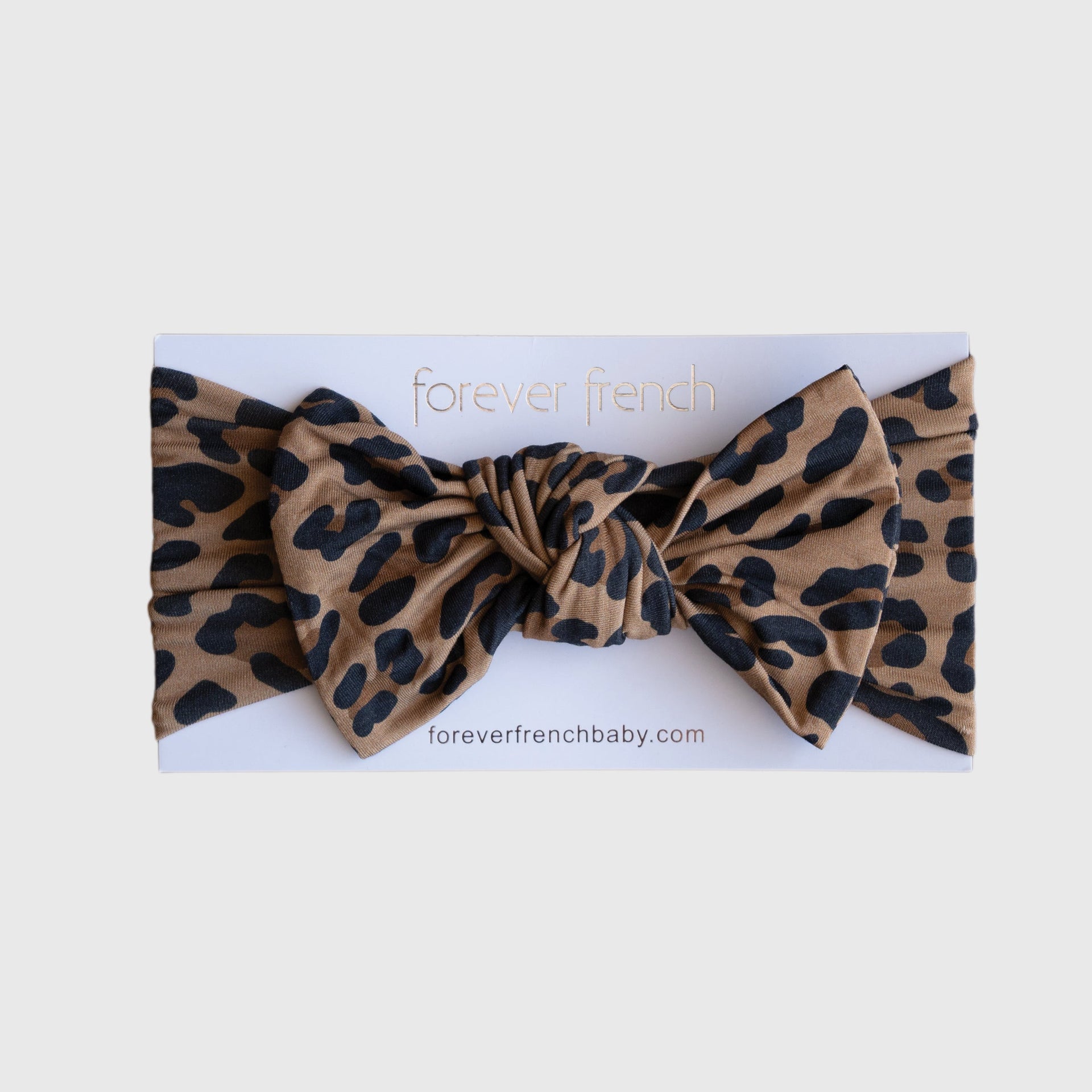 Baby wearing a silky-soft leopard print bamboo head wrap with a bow, classic tan and black pattern.