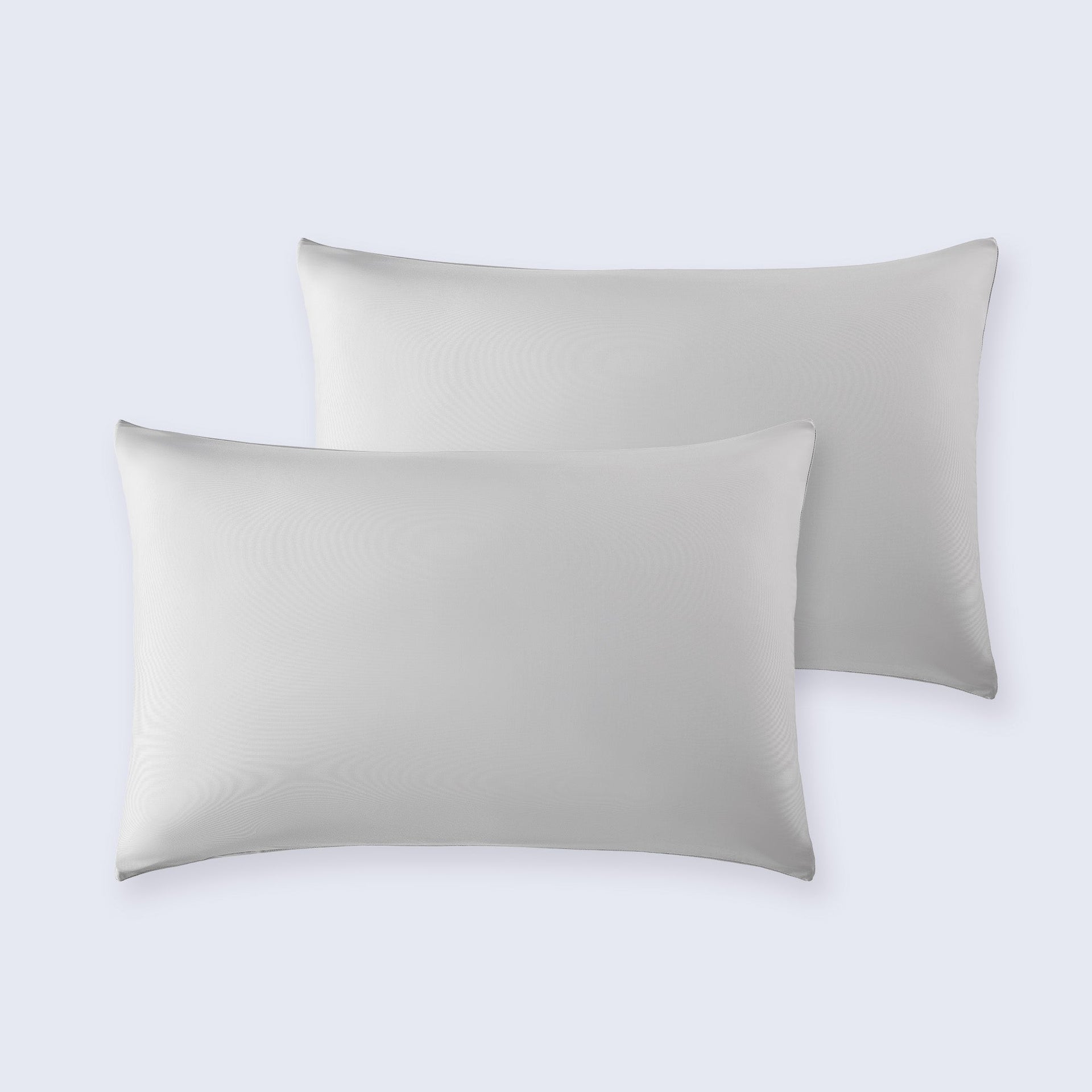 Set of two light grey cooling pillowcases on a white bed sheet.
