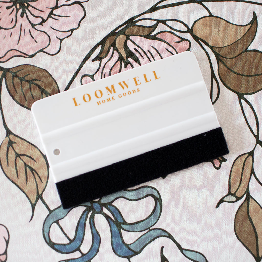 Monochrome 4-inch wallpaper squeegee with white plastic handle and black felt edge for scratch-free application.