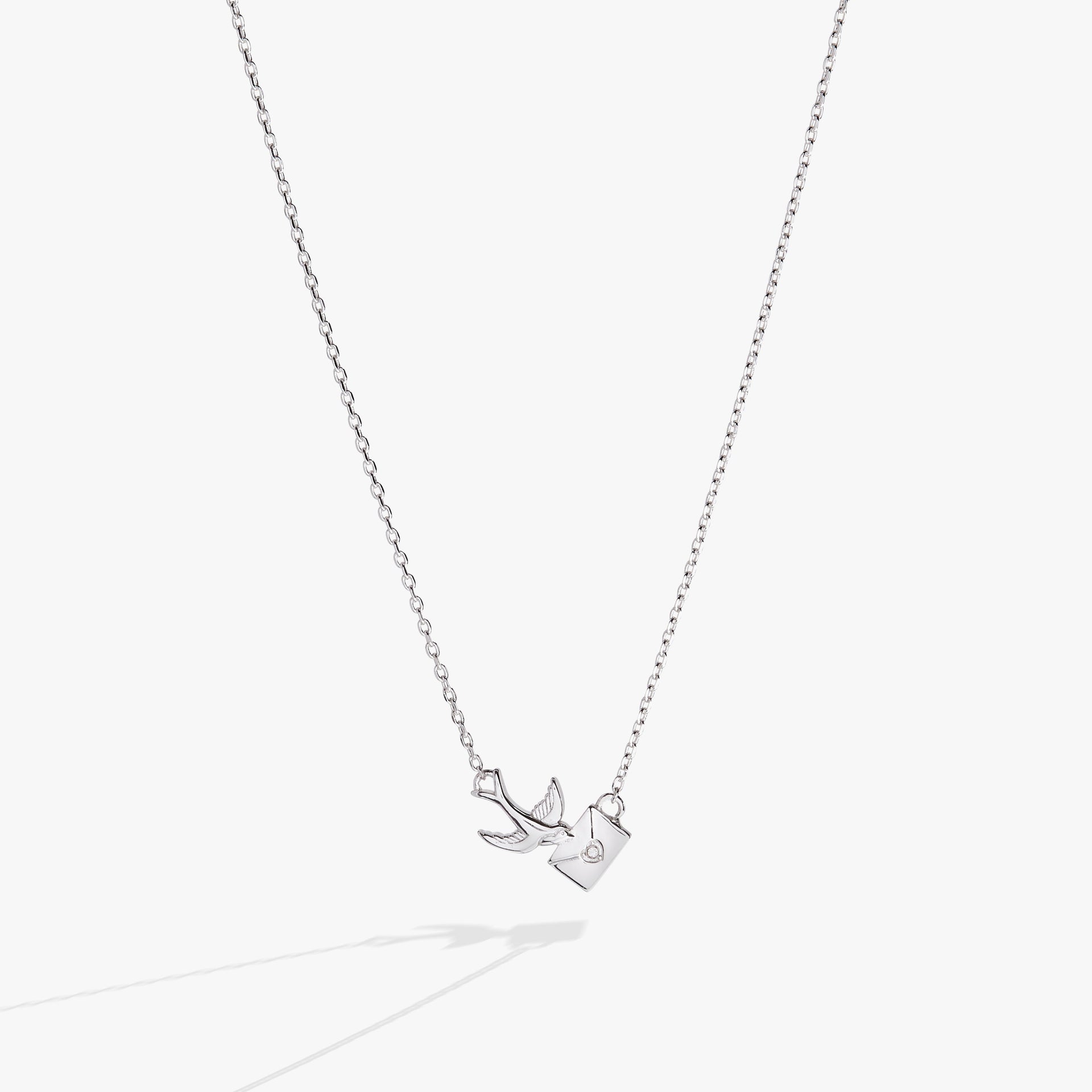 Delicate silver love letter pendant necklace featuring a swallow charm and a round crystal on a cable chain.