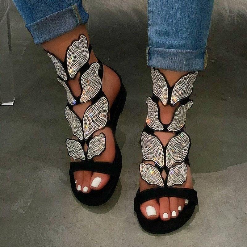 Close-up of women's flat sandals featuring rhinestone butterfly embellishment and soft leather finish