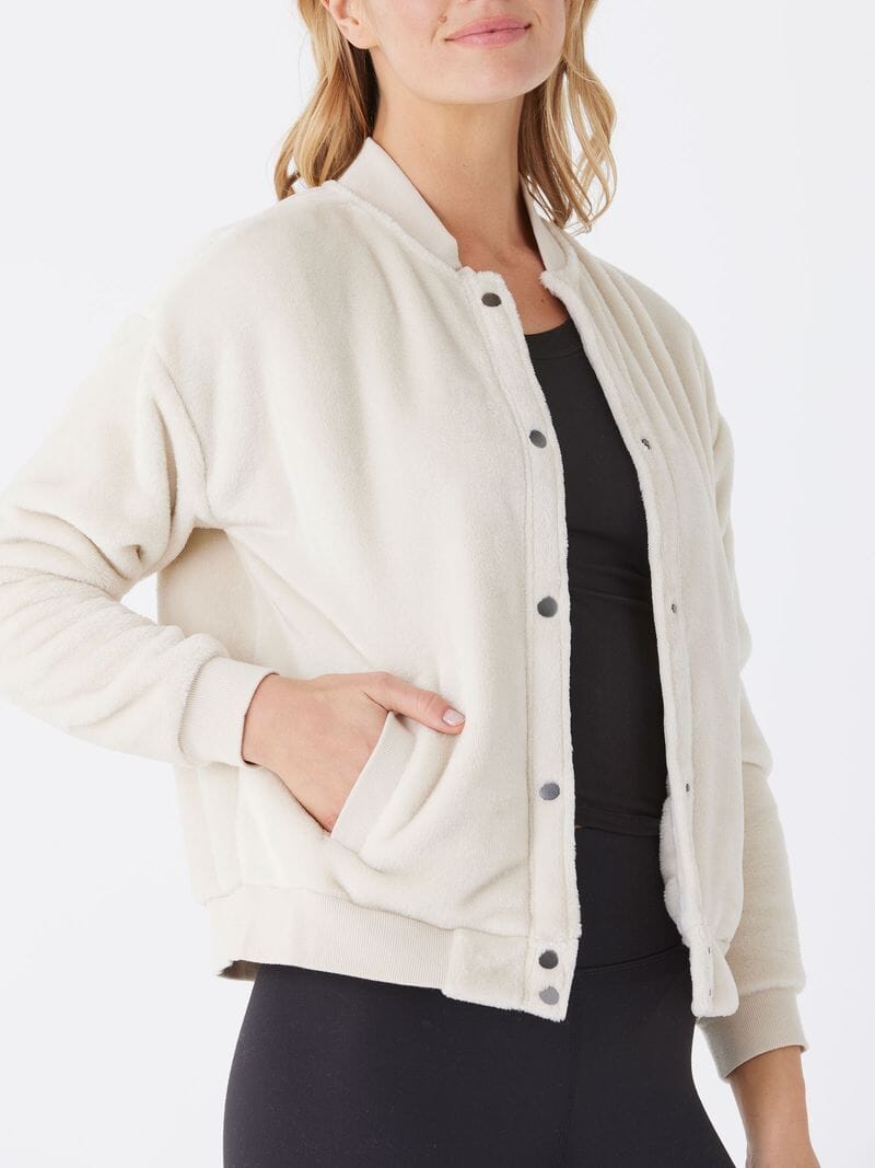A woman wearing a cozy off-white sherpa bomber jacket with a snap closure and collared neckline.