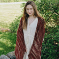Madeleine knit shawl in burgundy and copper tones draped over a surface