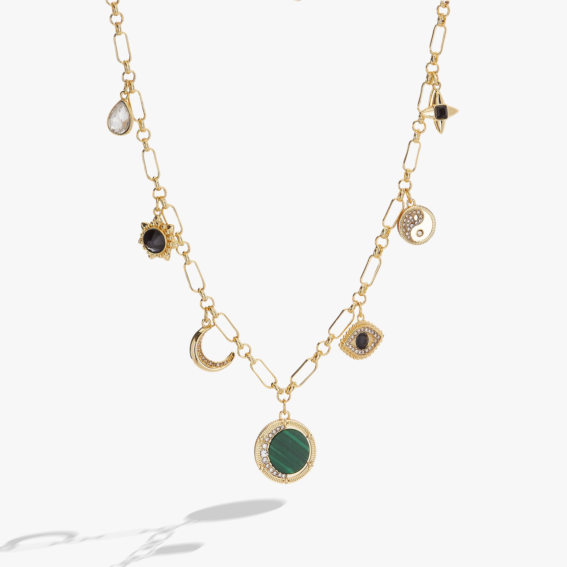 Gold-toned charm necklace featuring malachite stone, evil eye, yin-yang, and moon pendants
