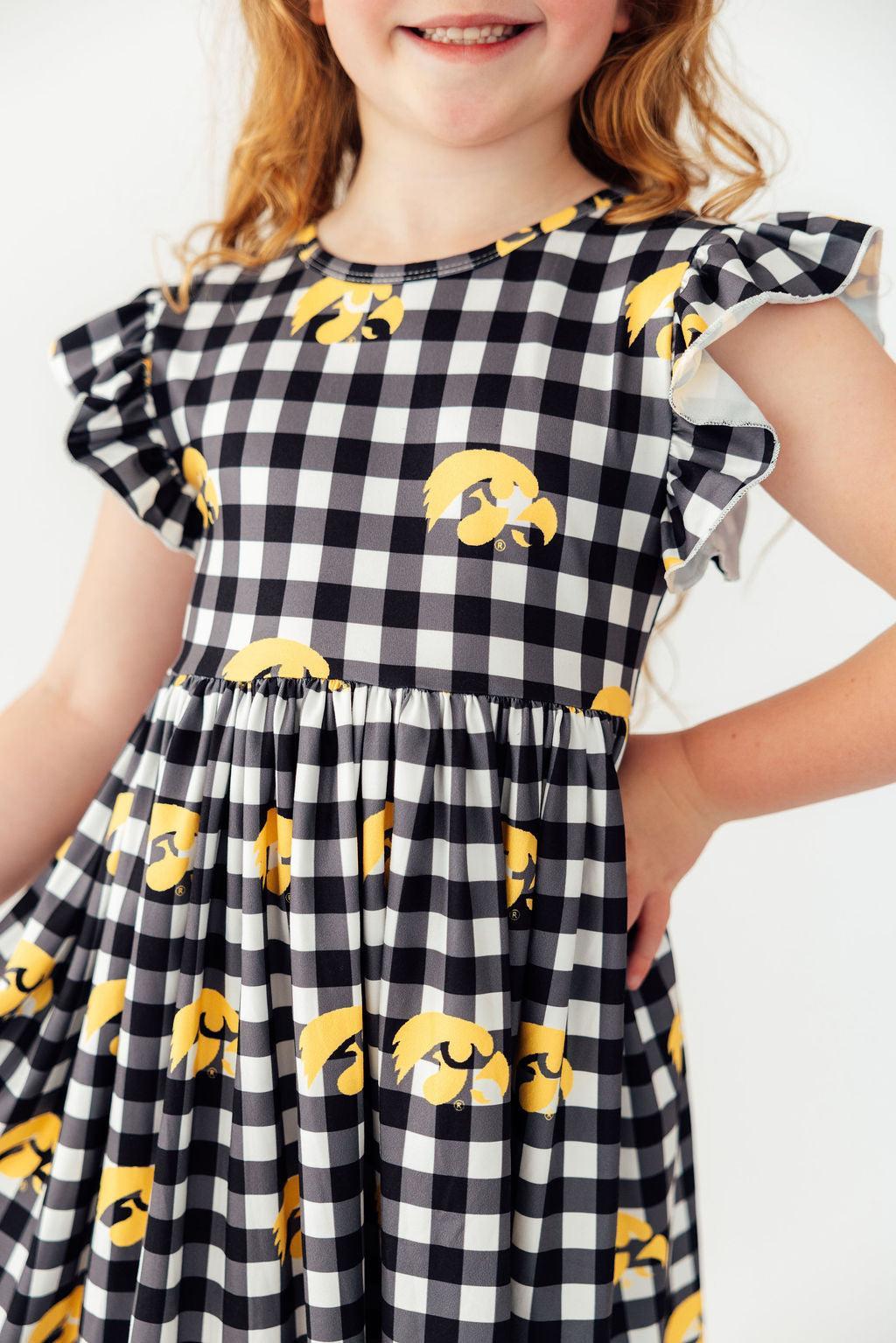 Young girl wearing black and white plaid dress with yellow Iowa Hawkeyes Tigerhawk logos and flutter sleeves