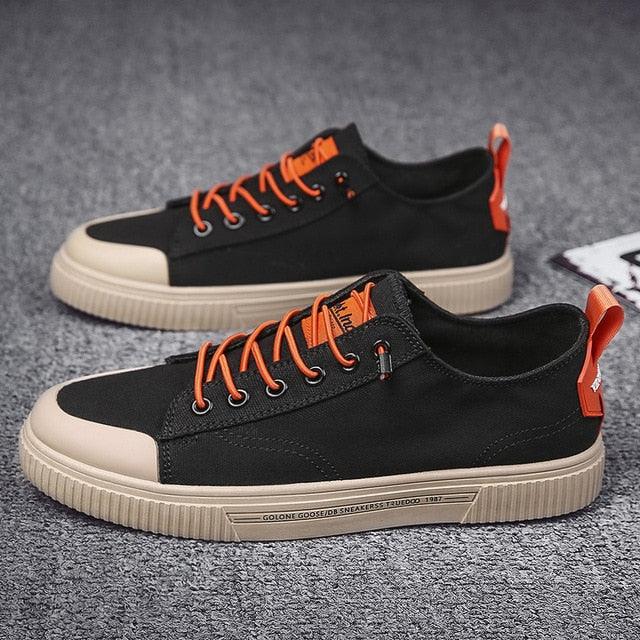 A pair of minimalist black and beige canvas lace-up sneakers for men on a neutral background.